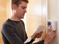 A man adjusting his home thermostat while reading his energy bill